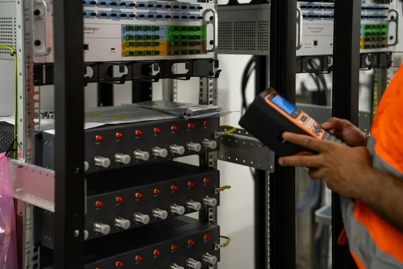 Technicien qui contrôle une baie réseau avec un appareil de mesure